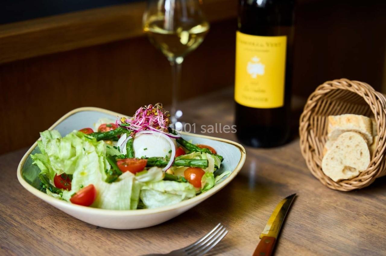 Salade fraîche avec légumes, radis et pousses, servie sur une table en bois avec pain, vin blanc et couteau.