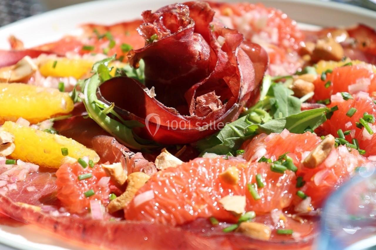 Assiette de carpaccio de bœuf garnie de roquette, agrumes, ciboulette et éclats de noix.