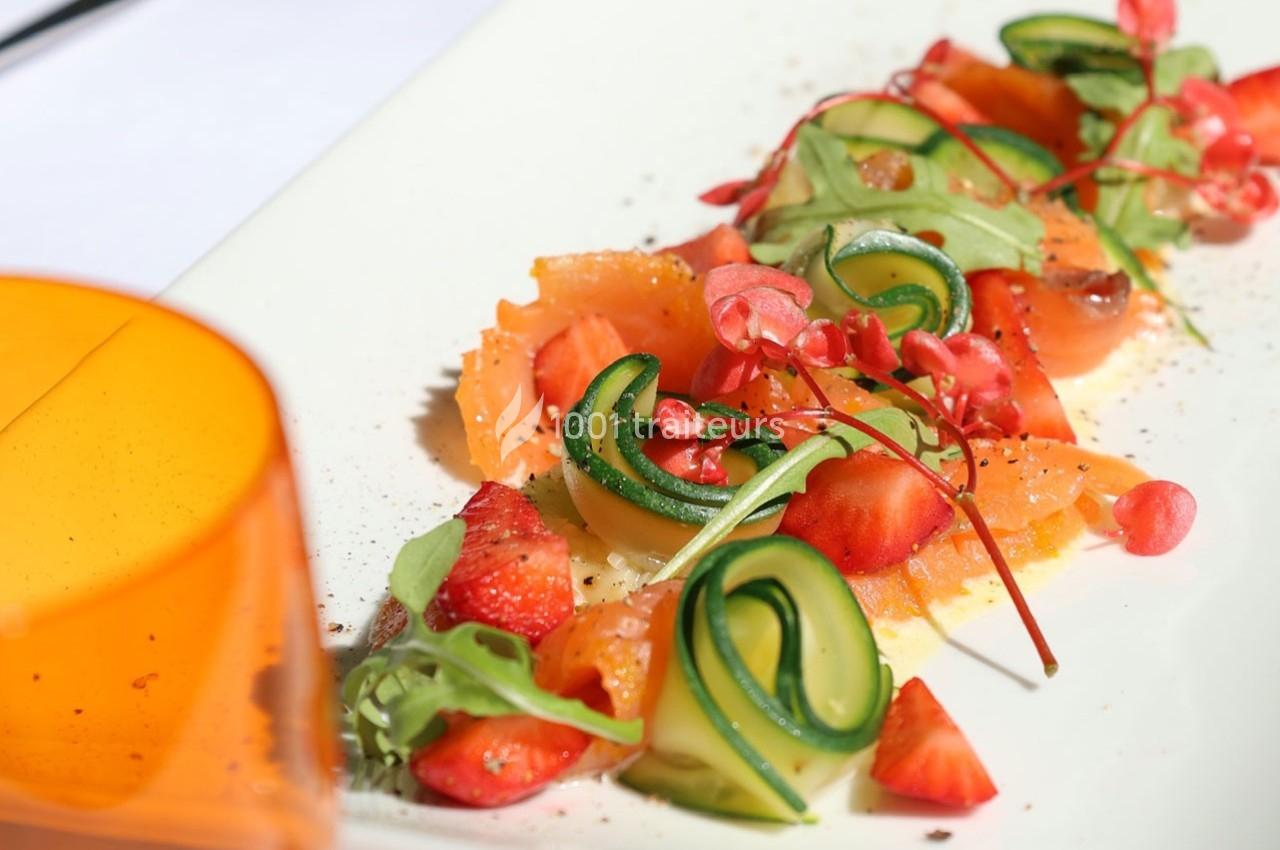 Assiette de saumon fumé avec des tranches de courgette, fraises, jeunes pousses et décoration colorée.