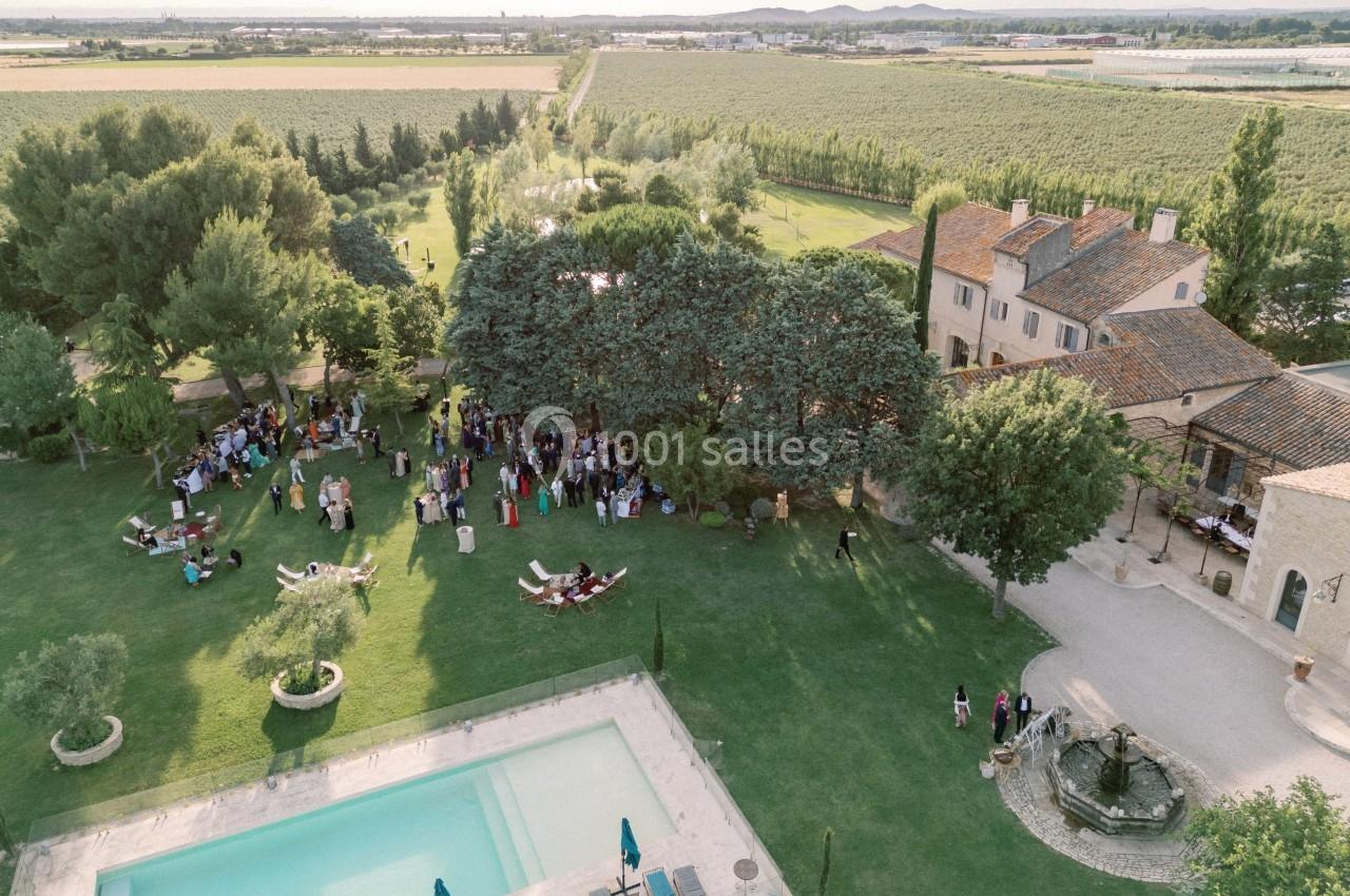 Vue aérienne d'un domaine avec piscine, jardins verdoyants, invités rassemblés et bâtiments en pierre.
