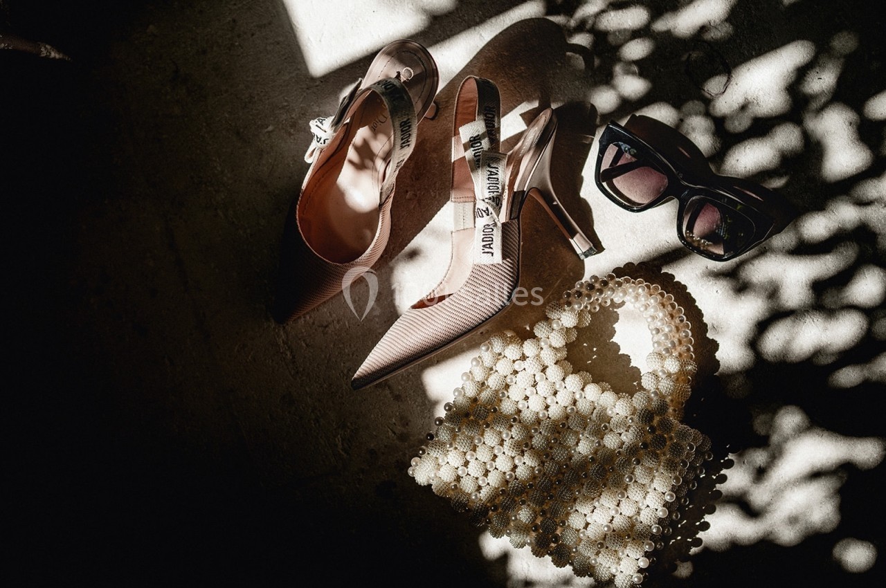 Chaussures à talons, lunettes de soleil et sac en perles posés sur un sol éclairé par une lumière tamisée.