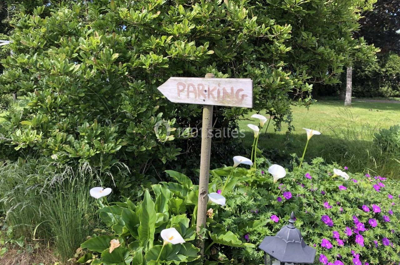 Panneau en bois indiquant ’Parking’ dans un jardin verdoyant avec des fleurs blanches et violettes.