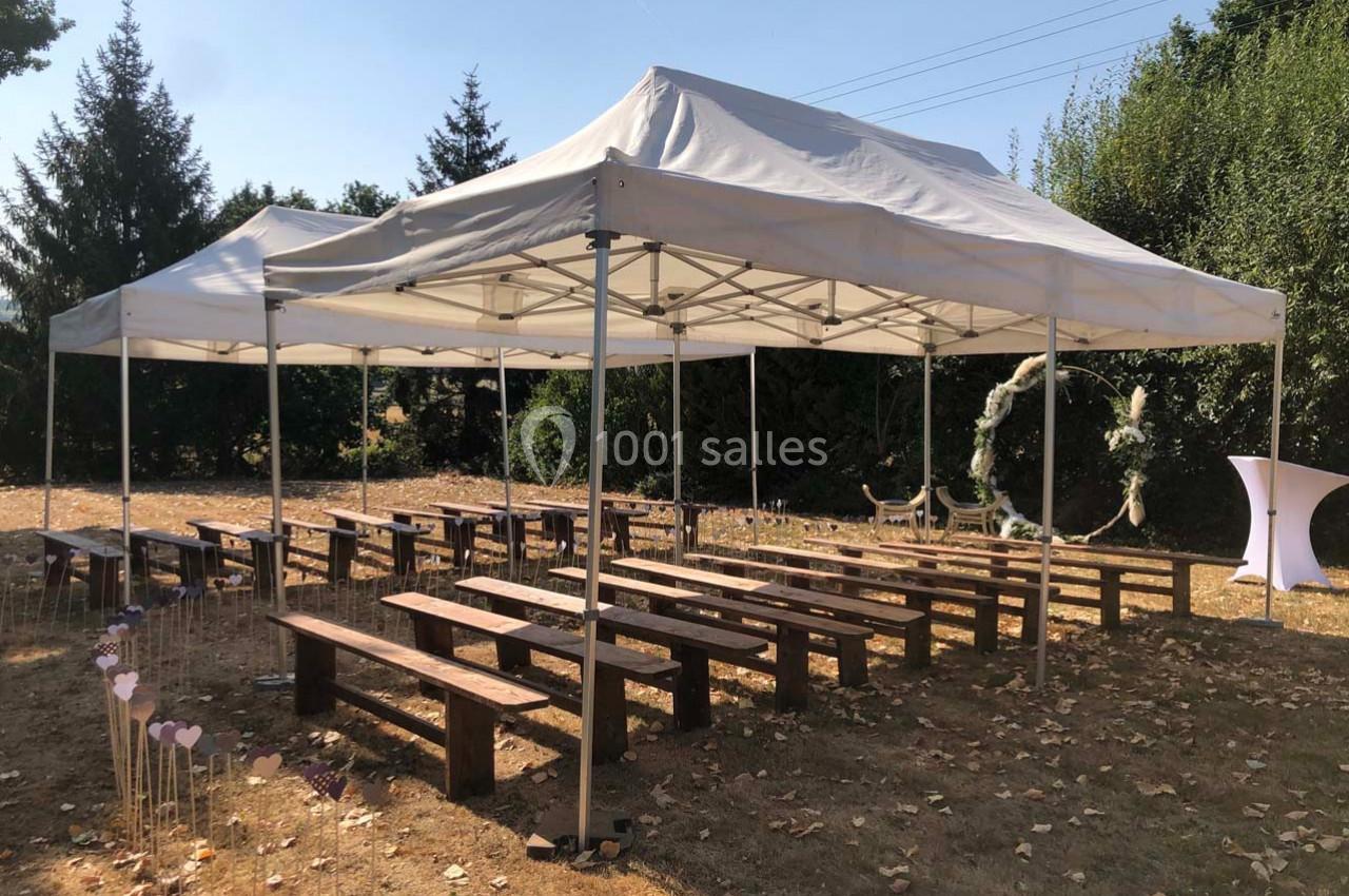 Tentes blanches montées sur une pelouse avec des bancs en bois disposés pour un événement en extérieur.