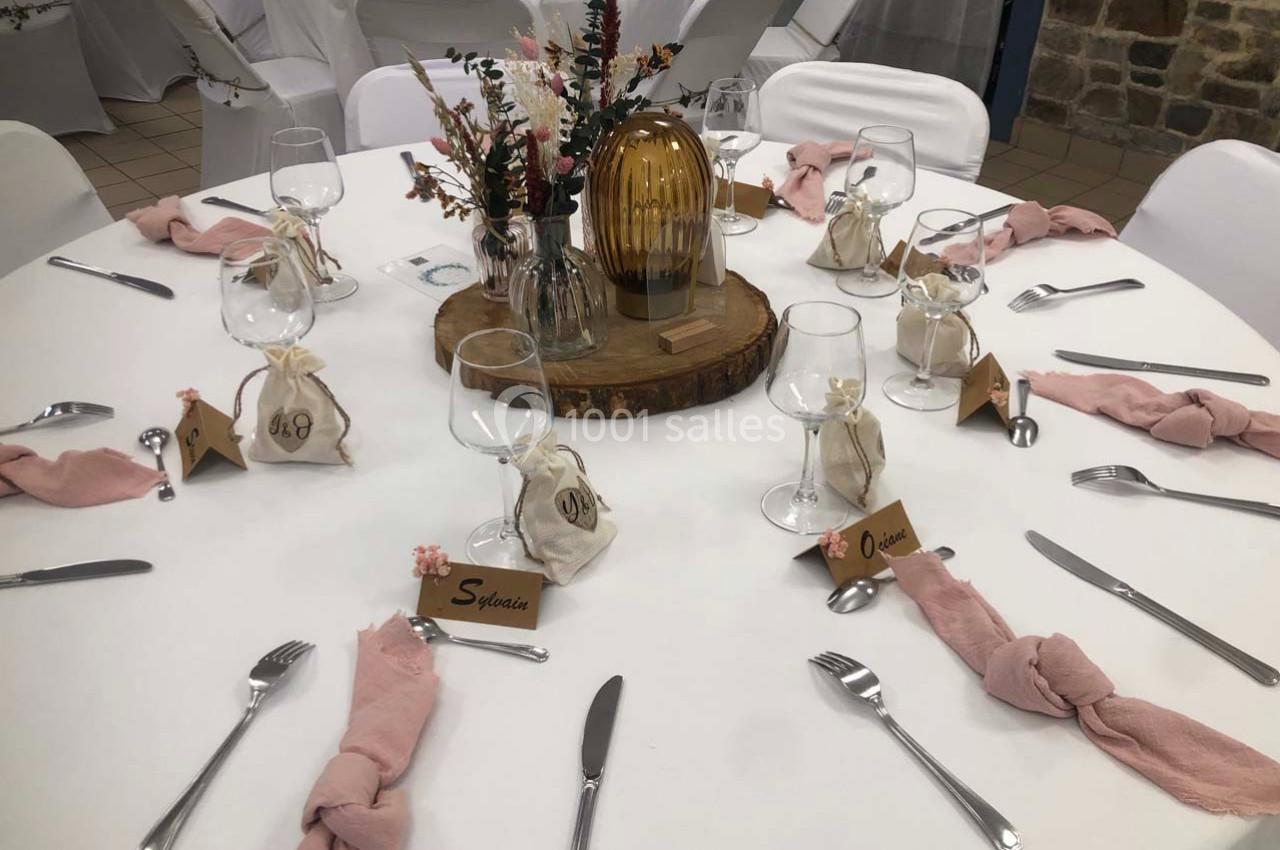 Table dressée avec nappes blanches, serviettes roses, centre de table floral et marque-places personnalisés.
