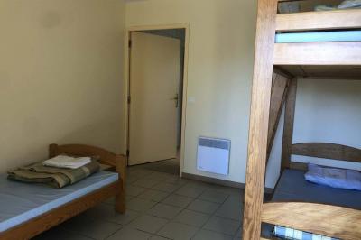 Dortoir avec plusieurs lits superposés en bois, matelas et oreillers, sur un sol carrelé clair.