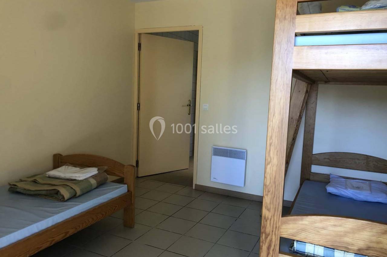 Chambre simple avec lit simple, lits superposés en bois, murs clairs, carrelage au sol et porte ouverte.