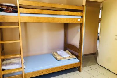 Dortoir avec plusieurs lits superposés en bois, matelas et oreillers, sur un sol carrelé clair.