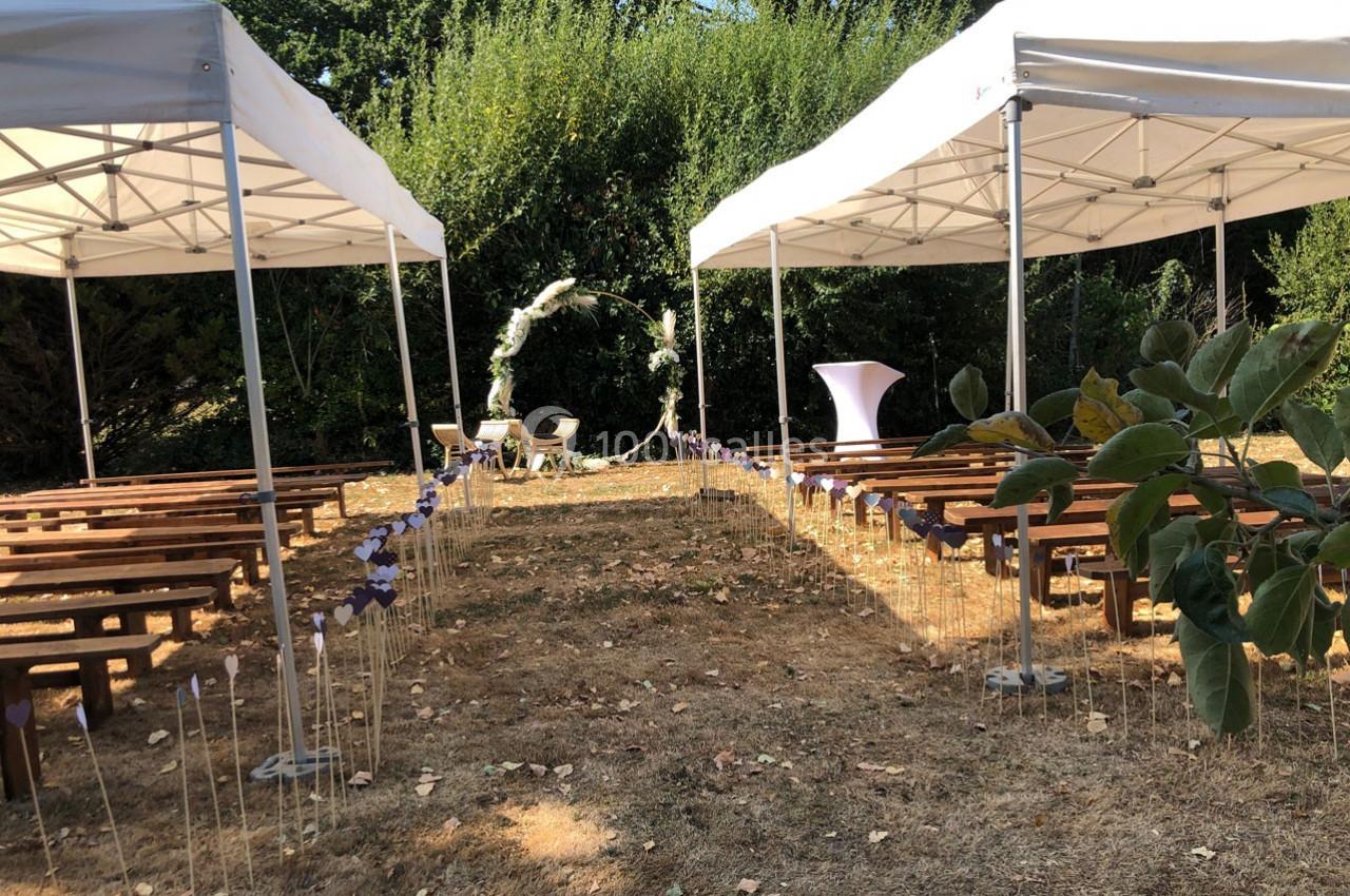 Allée centrale décorée pour une cérémonie en extérieur, entourée de bancs en bois et de tentes blanches.