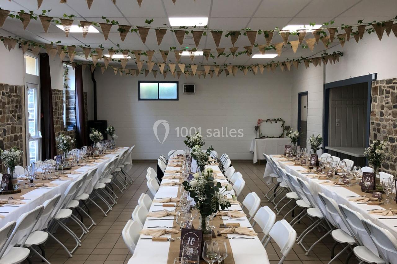Salle décorée pour un mariage avec longues tables dressées, guirlandes en tissu et compositions florales.