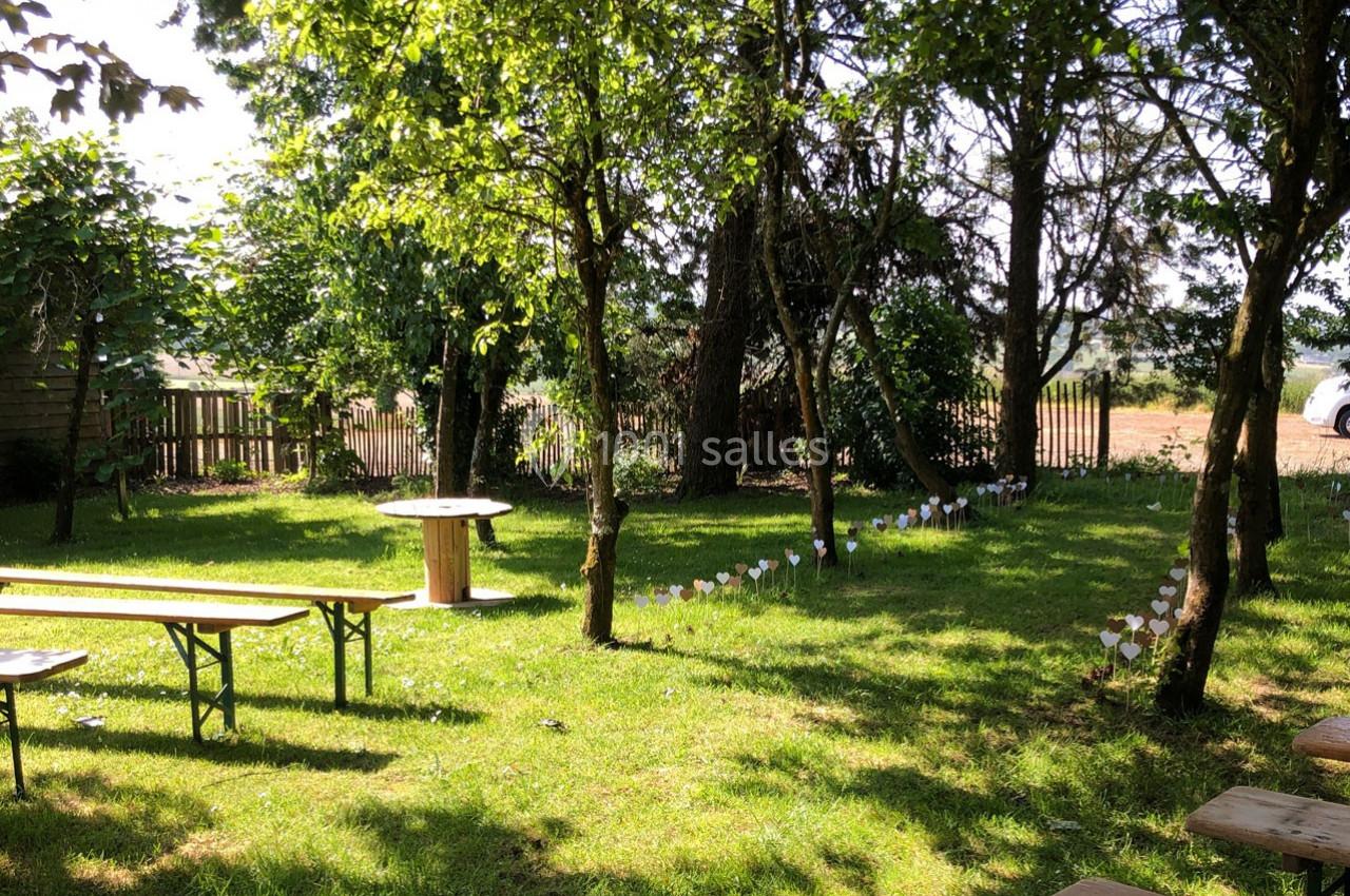 Un jardin ombragé avec des arbres, des bancs en bois et des décorations blanches plantées dans l'herbe.