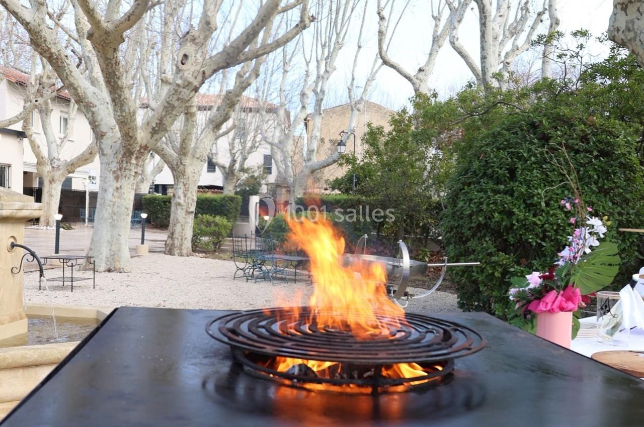 Flammes vives sur un gril en métal dans un espace extérieur bordé d'arbres et de bâtiments.