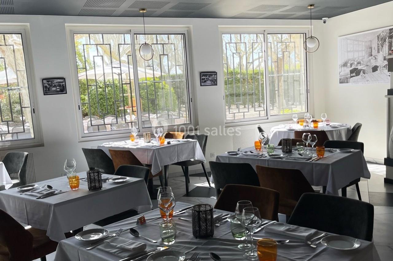 Salle de restaurant lumineuse avec des tables dressées, nappes blanches et grandes fenêtres donnant sur l'extérieur.