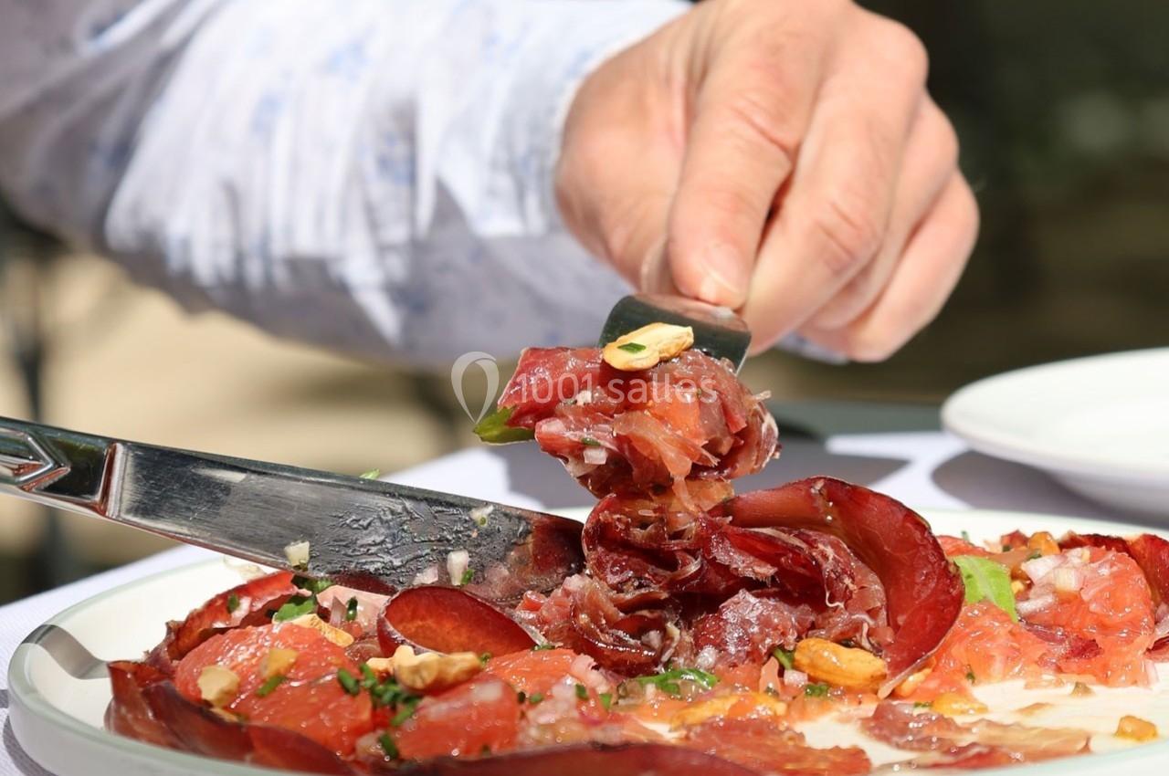 Une main utilise un couteau pour servir des tranches fines de viande séchée garnies de noix et d'herbes.