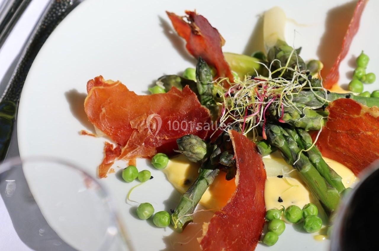 Assiette garnie d'asperges, petits pois, jambon cru croustillant et sauce crémeuse, décorée de pousses germées.