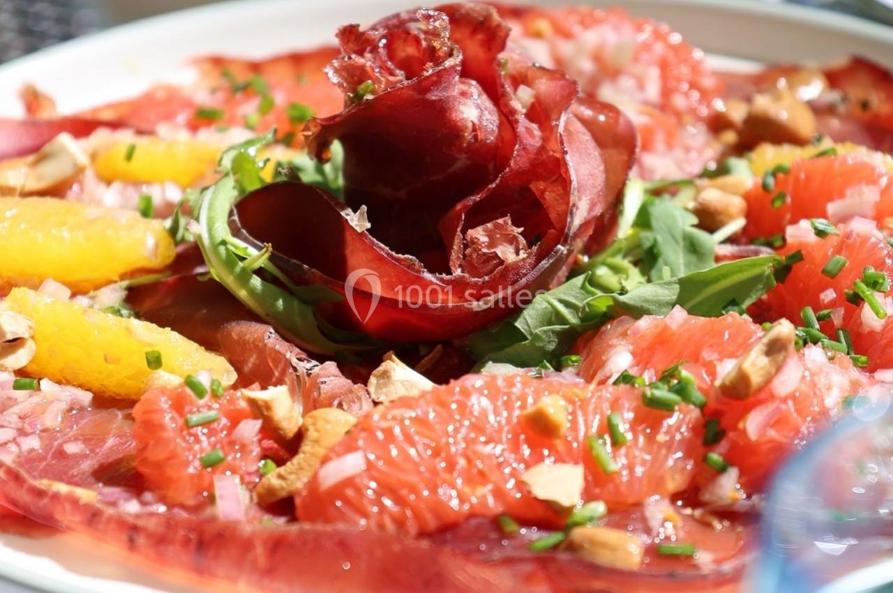 Assiette de carpaccio de viande séchée garnie de pamplemousse, roquette, noix et ciboulette.