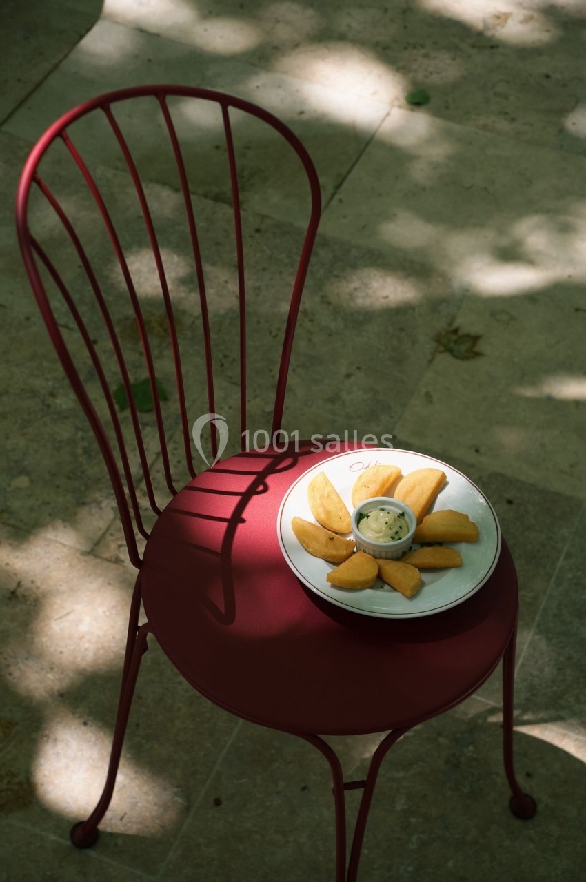 Assiette de beignets disposés en cercle avec une sauce au centre, posée sur une chaise rouge en métal.