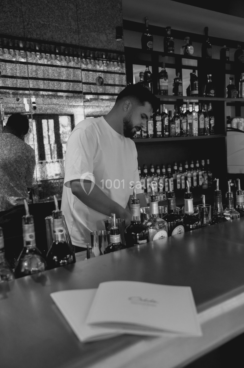 Un barman prépare des boissons derrière un comptoir, entouré de bouteilles d'alcool, dans un bar moderne.