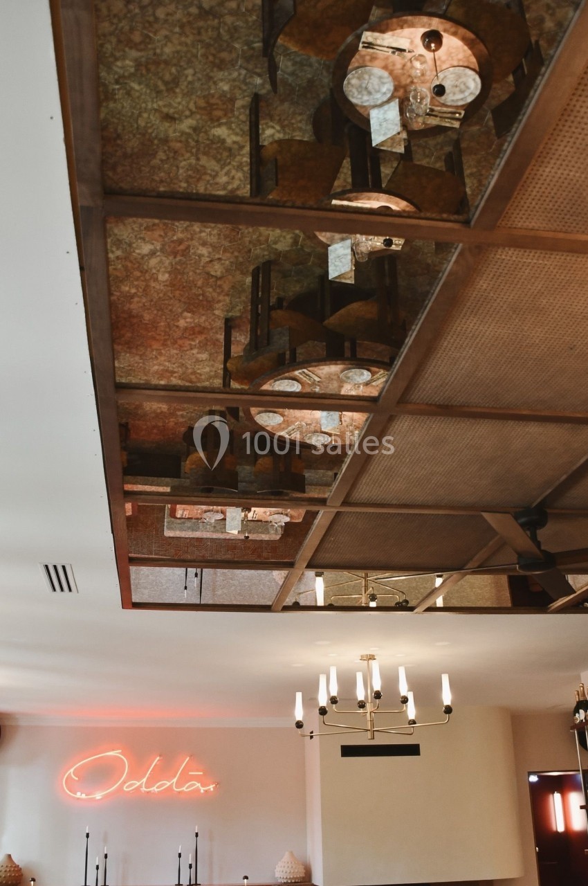 Plafond avec miroir reflétant des luminaires suspendus et un mur avec une enseigne lumineuse rouge.