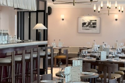 Table dressée avec assiettes, couverts, verres, serviettes et menu sur un set de table rond dans un restaurant.