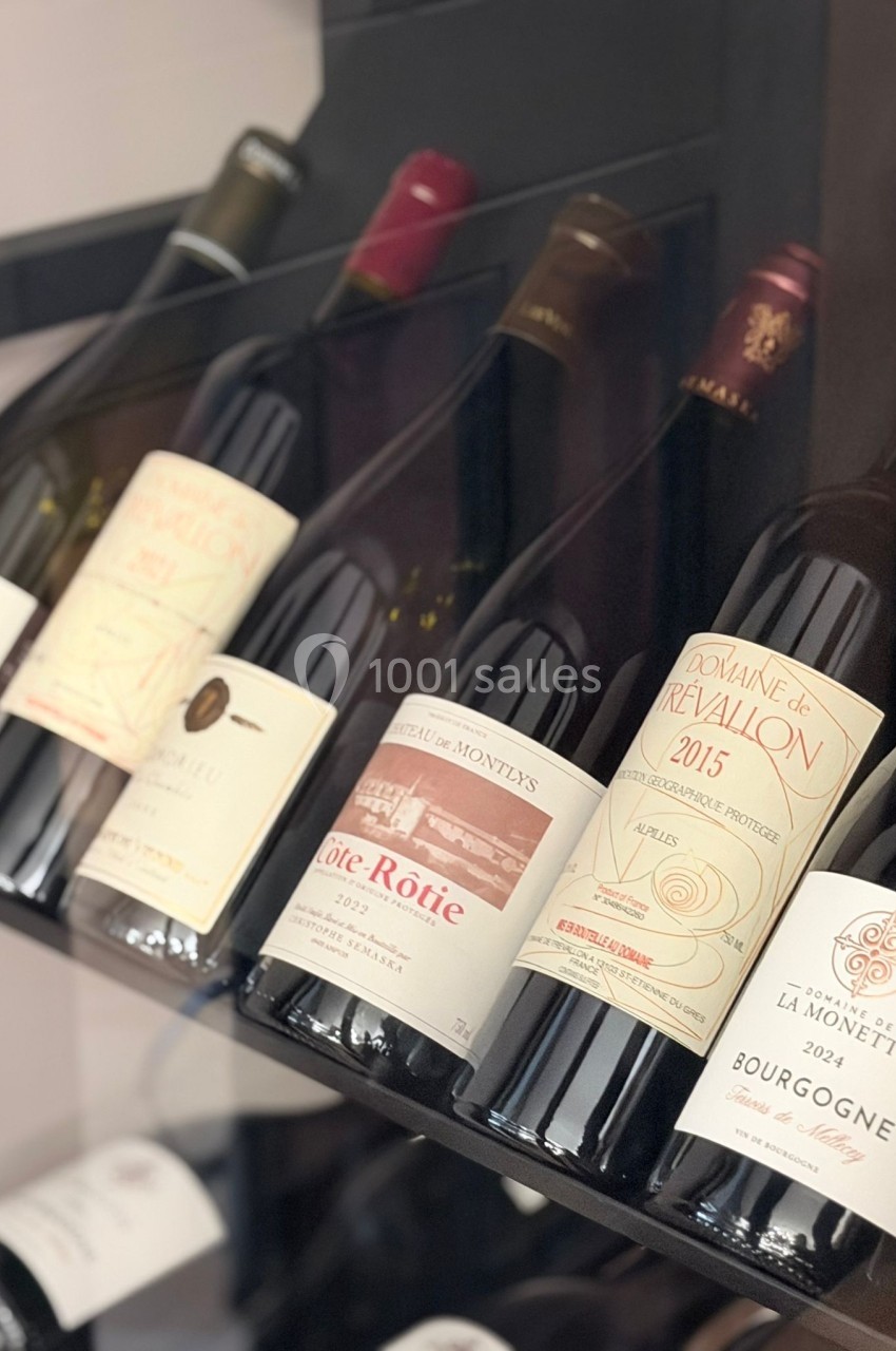 Bouteilles de vin rouge et blanc alignées sur une étagère, étiquettes visibles avec différentes appellations françaises.