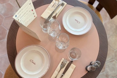 Table dressée avec assiettes, couverts, verres, serviettes et menu sur un set de table rond dans un restaurant.