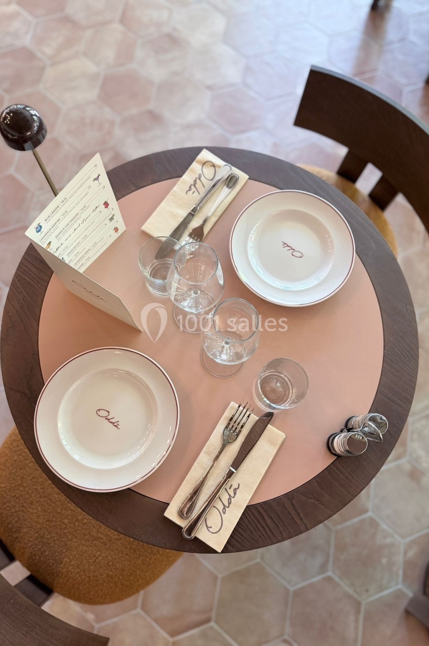 Table dressée avec assiettes, couverts, verres, serviettes et menu sur un set de table rond dans un restaurant.