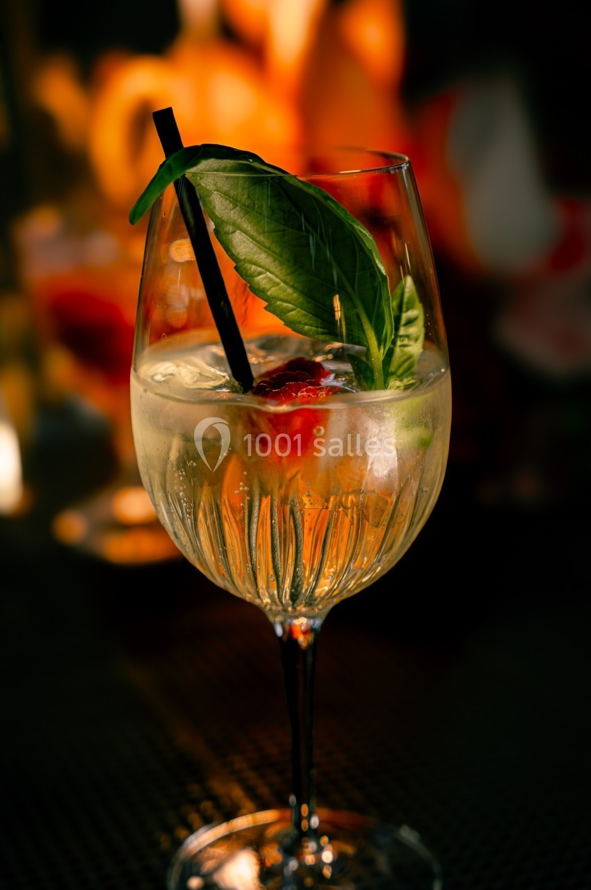 Verre de cocktail garni de feuilles de basilic, d'une paille noire et de fruits, posé sur une table sombre.