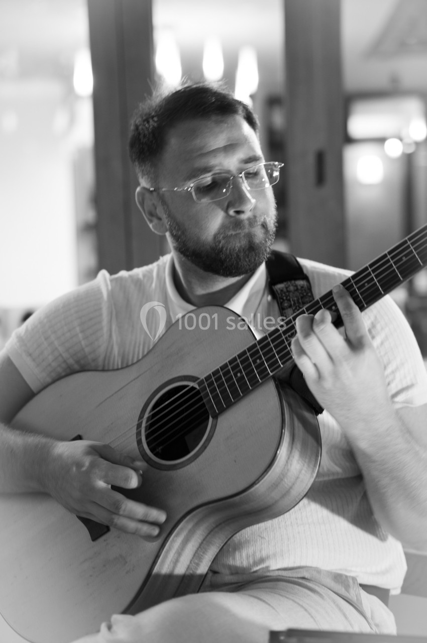 Un homme joue de la guitare acoustique dans un intérieur éclairé, capturé en noir et blanc.