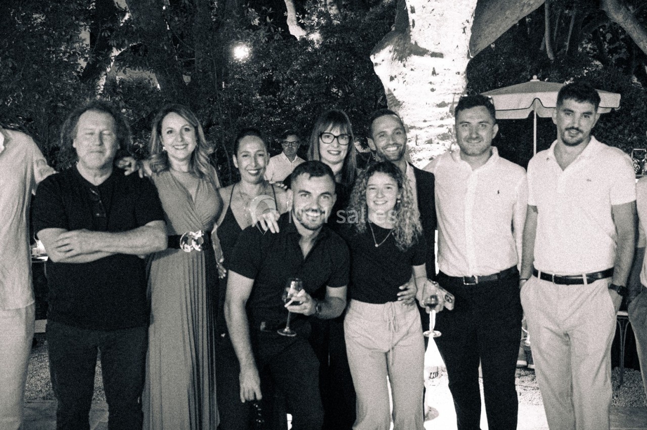 Un groupe de personnes posant ensemble en extérieur, sous des arbres, lors d'un événement en soirée.