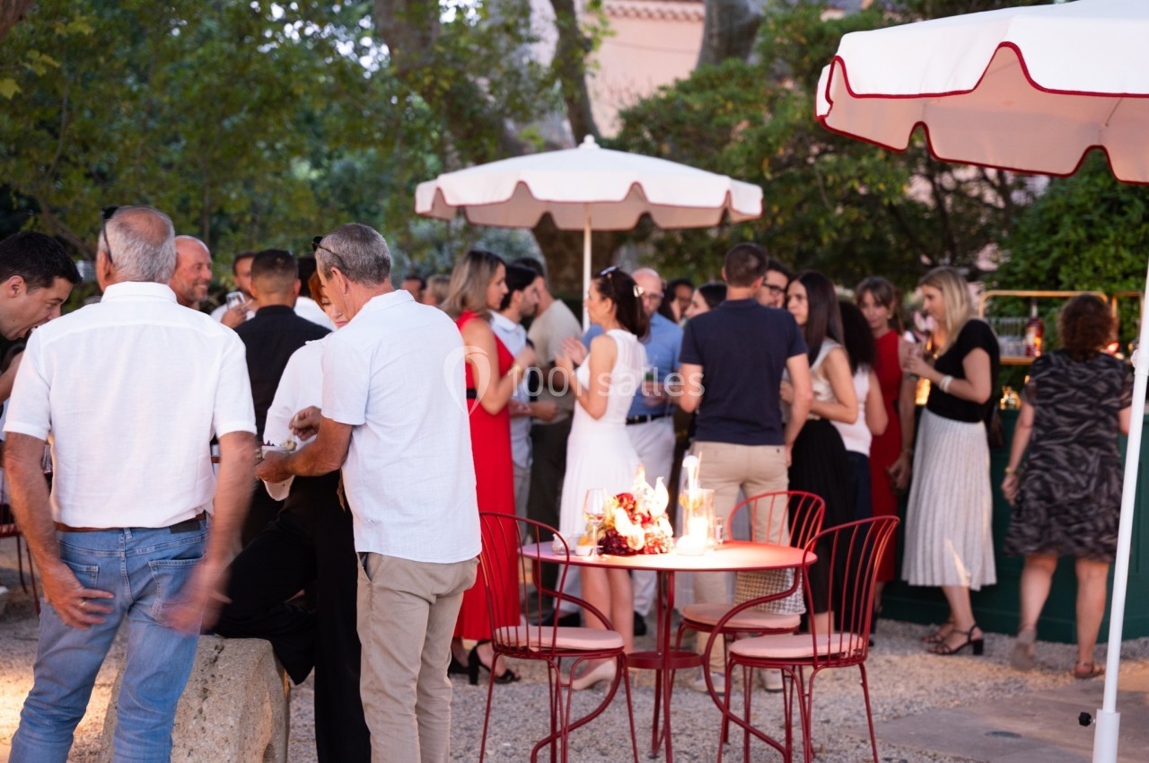 Groupe de personnes discutant et partageant un moment convivial dans un jardin avec des tables et parasols.