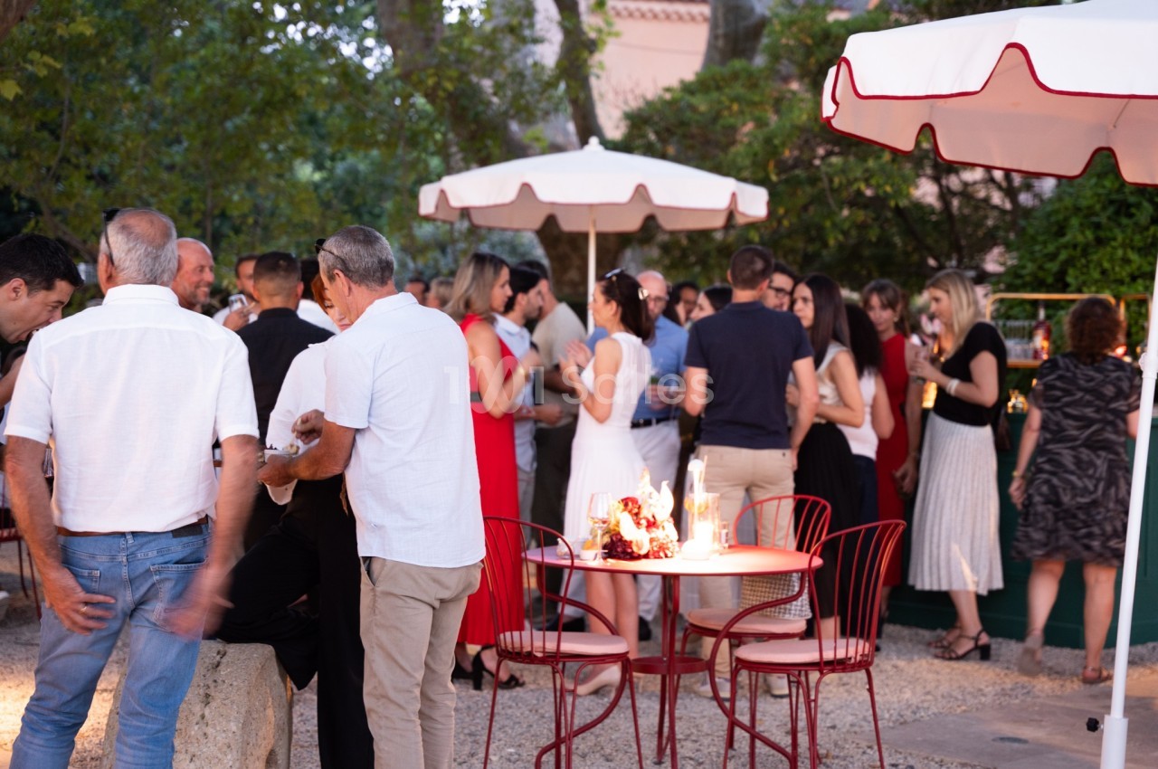 Groupe de personnes discutant et partageant un moment convivial dans un jardin avec des tables et parasols.