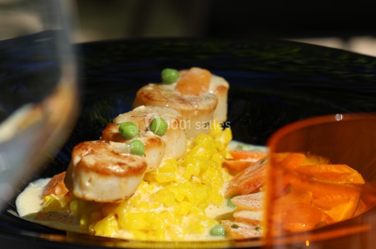 Assiette de risotto au safran, noix de Saint-Jacques poêlées et petits pois, servie avec des légumes en accompagnement.