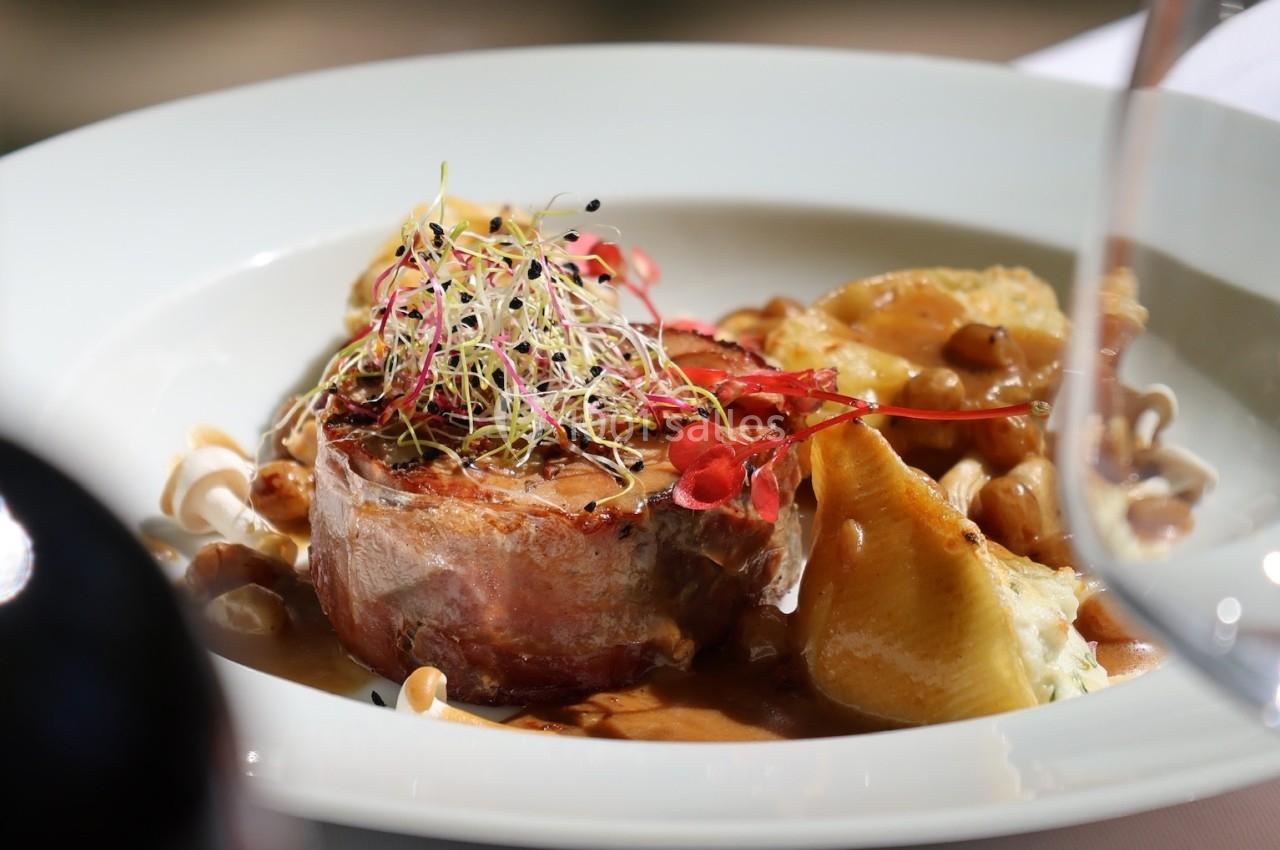 Assiette gastronomique avec viande en sauce, légumes, germes décoratifs et verre de vin en arrière-plan flou.