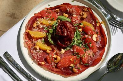 Panier en osier rempli de fruits variés, dont ananas, pommes, oranges et citrons, posé sur une nappe blanche.