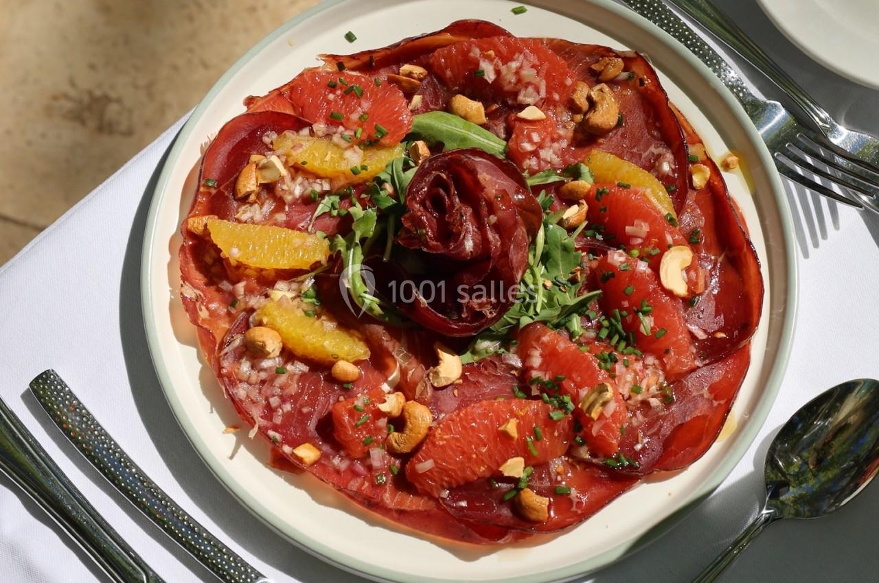 Assiette de carpaccio de bœuf garnie d'agrumes, noix de cajou et herbes fraîches, servie sur une table dressée.