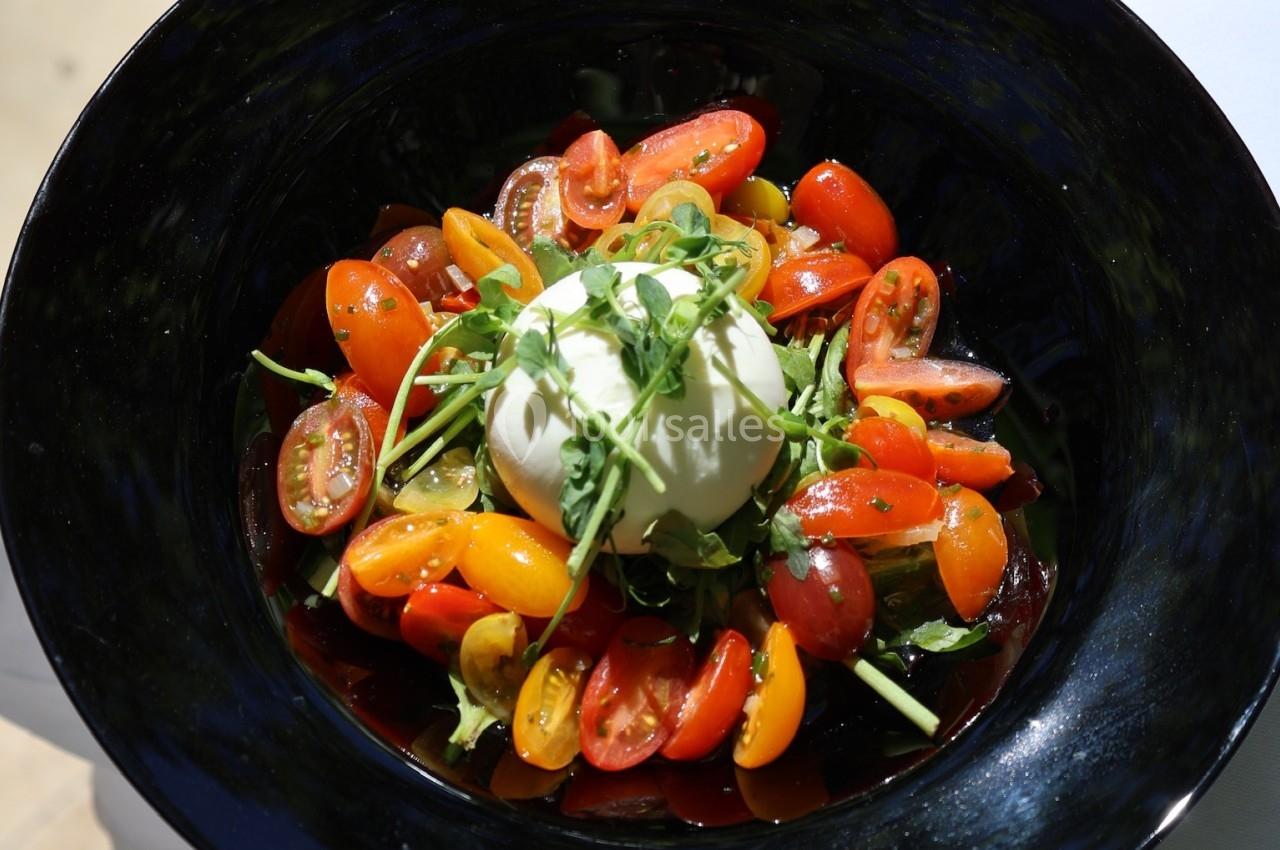 Assiette de burrata garnie de tomates cerises colorées et de roquette, présentée sur une table en extérieur.