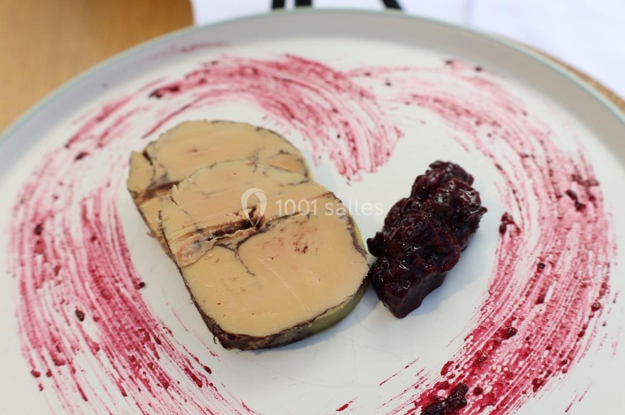 Tranche de foie gras accompagnée d'une confiture de fruits rouges, présentée sur une assiette décorée de coulis.