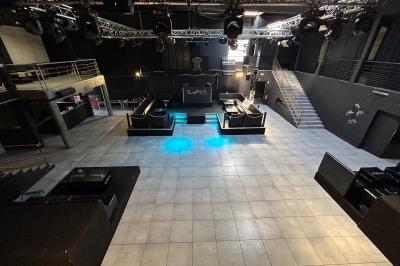 Espace lounge sombre avec canapés en cuir, tables basses marquées ’Cîroc’ et décoration lumineuse en forme d'astronaute.