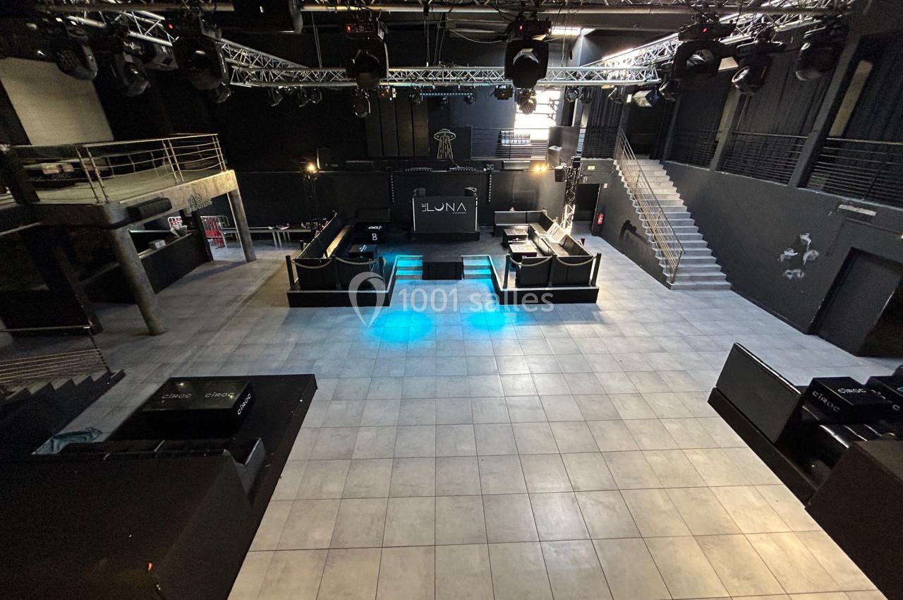 Salle de concert vide avec scène centrale, éclairages suspendus et escaliers menant à une mezzanine.