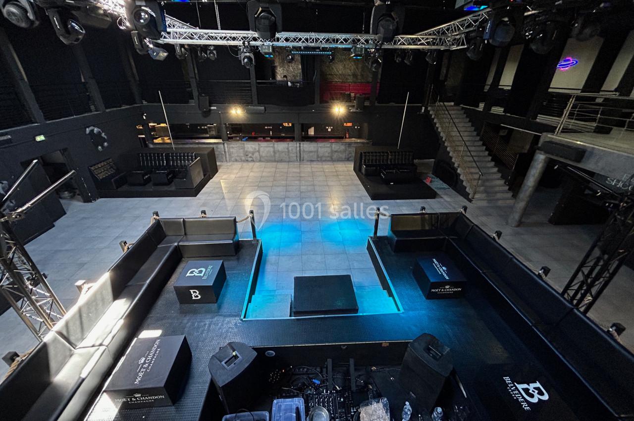 Vue d'une salle de spectacle vide avec scène centrale, piste de danse, estrades et équipements techniques.