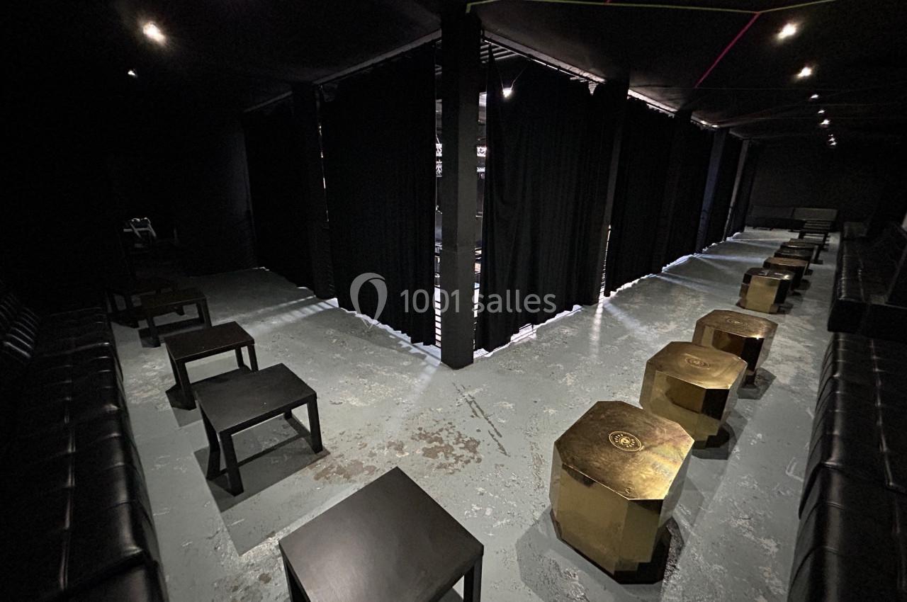 Salle sombre avec tables noires, tabourets dorés et rideaux noirs séparant l’espace.