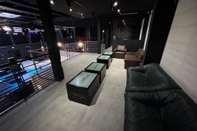 Espace lounge sombre avec canapés en cuir, tables basses marquées ’Cîroc’ et décoration lumineuse en forme d'astronaute.