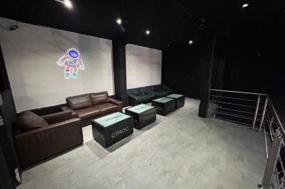 Espace lounge sombre avec canapés en cuir, tables basses marquées ’Cîroc’ et décoration lumineuse en forme d'astronaute.