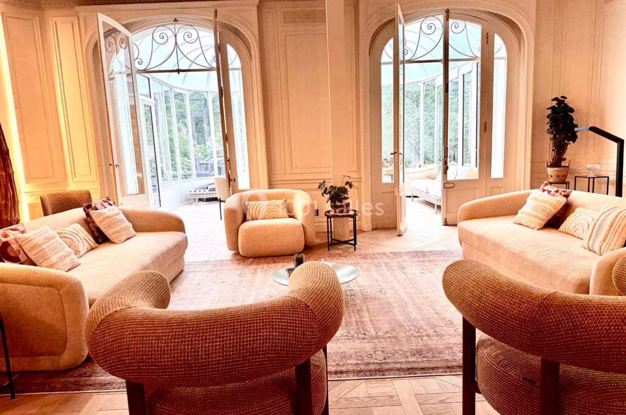 Salon lumineux avec mobilier beige, grandes portes vitrées ouvertes sur une véranda et vue sur un jardin verdoyant.