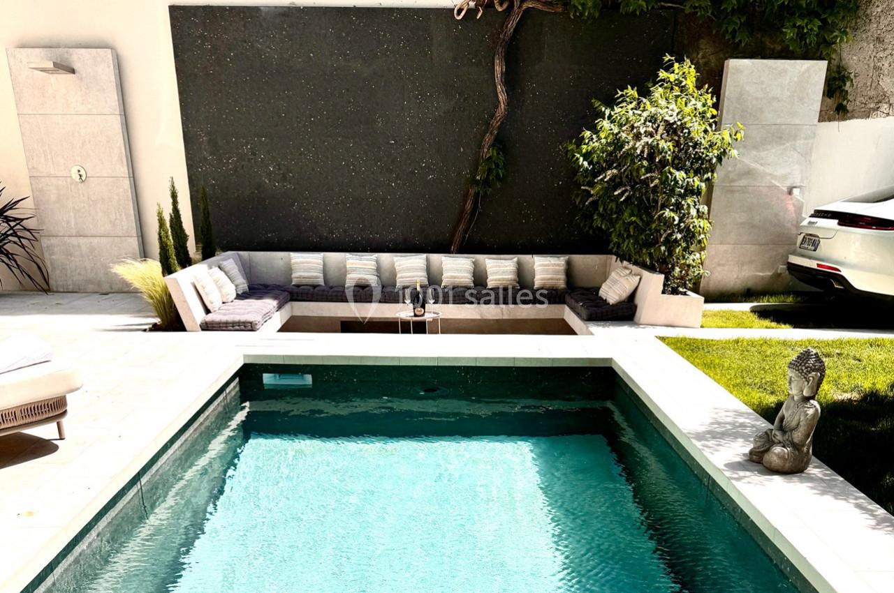 Piscine extérieure entourée de verdure, avec un coin salon moderne et une statue décorative au bord de l'eau.