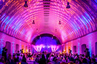 Salle avec des murs en pierre et poutres apparentes, aménagée pour une cérémonie avec des invités assis sur des chaises…