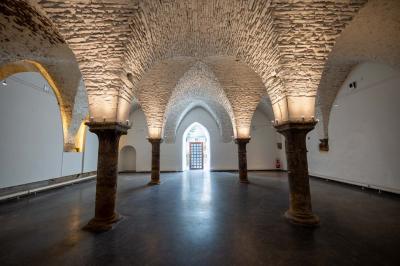 Salle avec des murs en pierre et poutres apparentes, aménagée pour une cérémonie avec des invités assis sur des chaises…