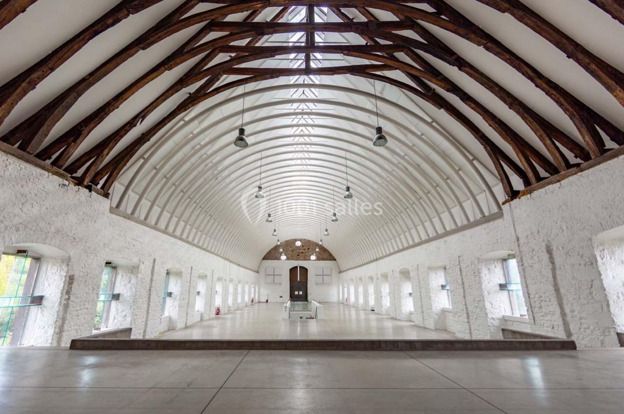 Grande salle voûtée avec poutres en bois apparentes, murs blancs en pierre et fenêtres alignées sur les côtés.