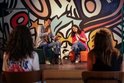 Un couple célèbre son mariage sur une petite scène décorée de voiles et de feuillages, devant une fresque colorée.