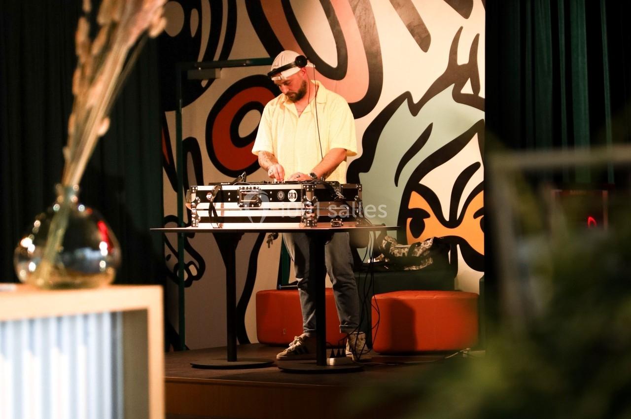 Un DJ mixe sur une table de mixage dans un espace intérieur décoré avec des motifs muraux colorés.
